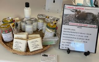 A display of goat milk lotions and soaps for sale with a price list at carmel gardens.